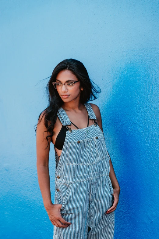 a  in glasses and overalls leaning against a wall