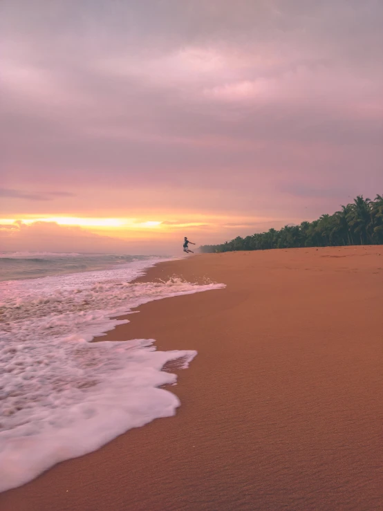 a person stands at the shore of a beach as the sun sets