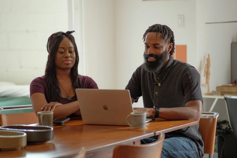 a man and woman are sitting at a desk looking on their laptop