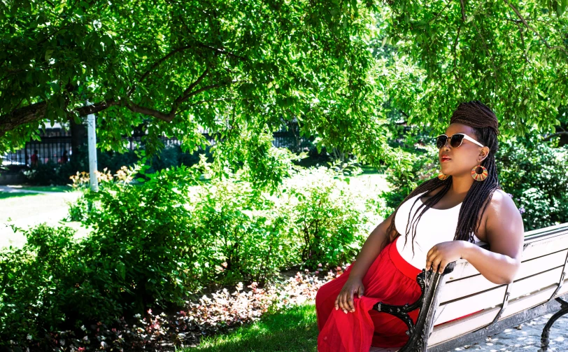 a woman is sitting on a park bench near some bushes