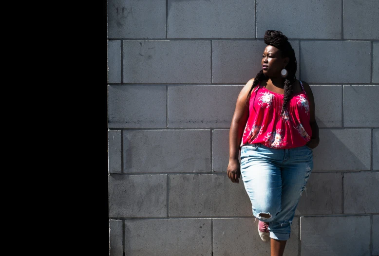 an african american woman standing by a gray brick wall