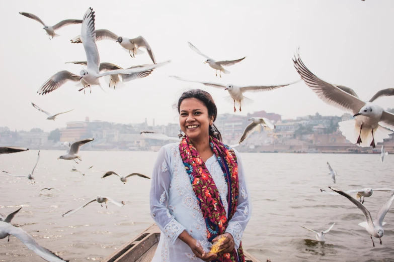 an attractive woman standing by the ocean with seagulls surrounding her