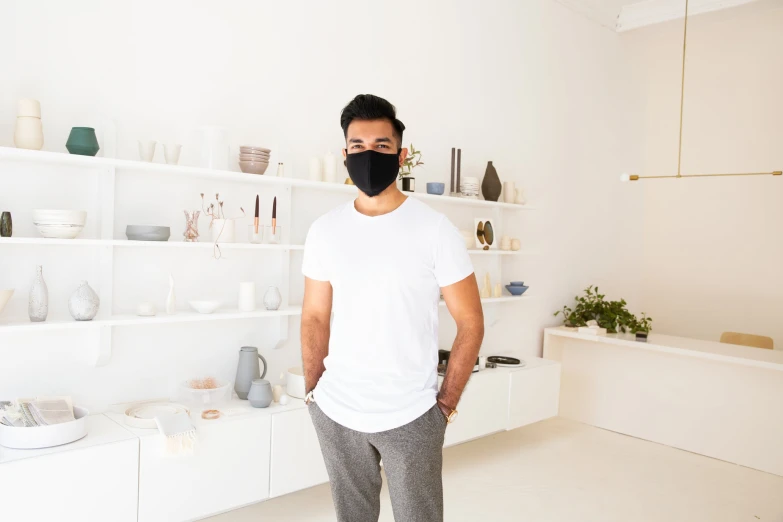 man standing in front of white shelves with plants and vases