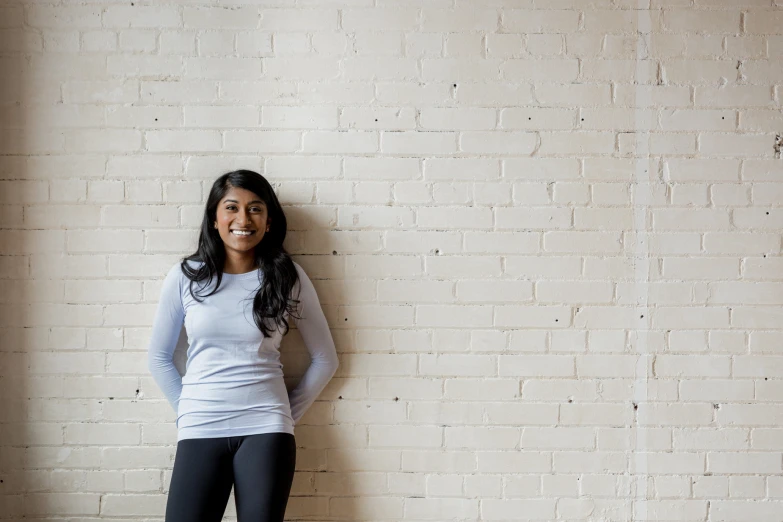 a woman wearing black leggings stands in front of a brick wall