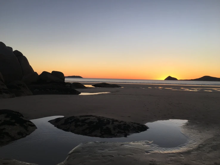 the sun setting on an ocean beach near many rocks