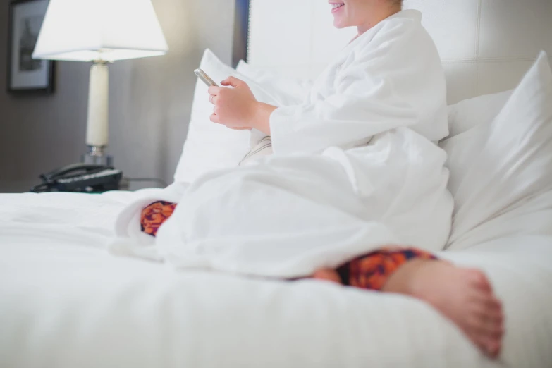 a woman in white pajamas sits on her bed