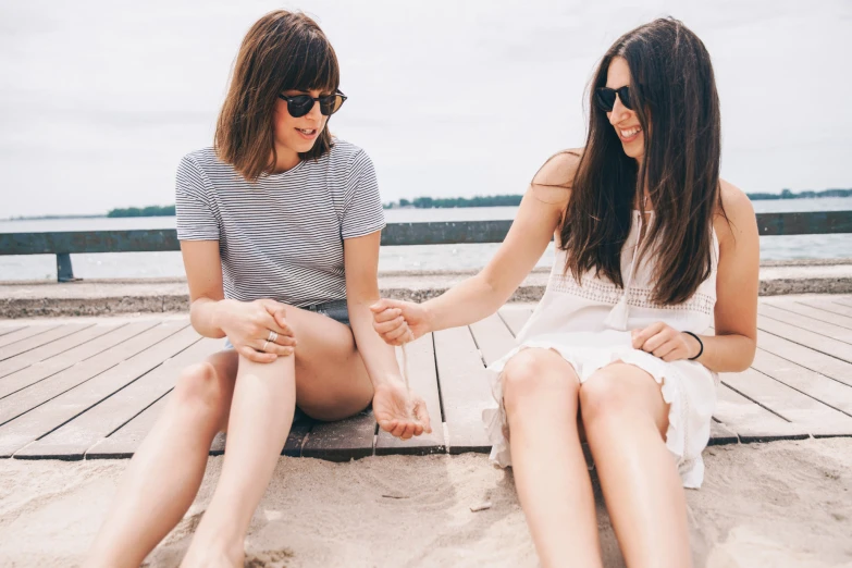 two girls sitting on a dock at the water