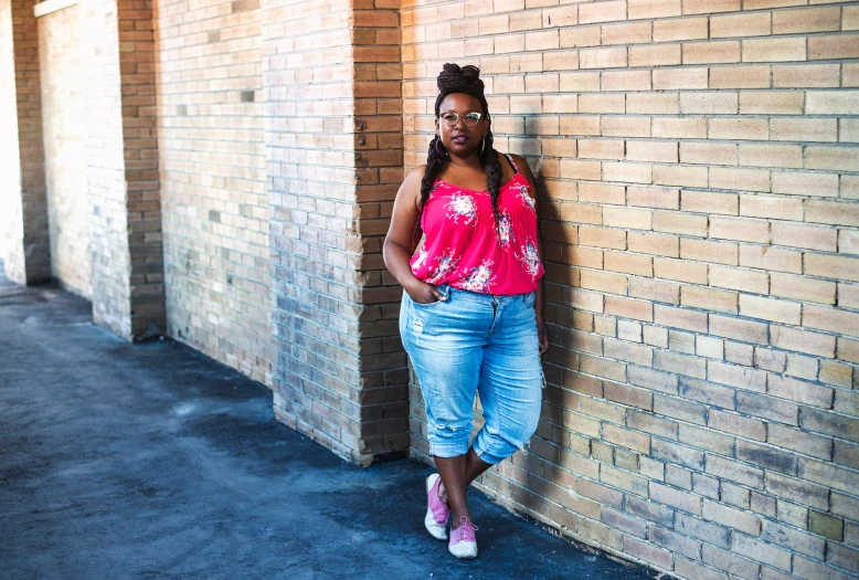 a black woman leaning against a brick wall, leaning on a building