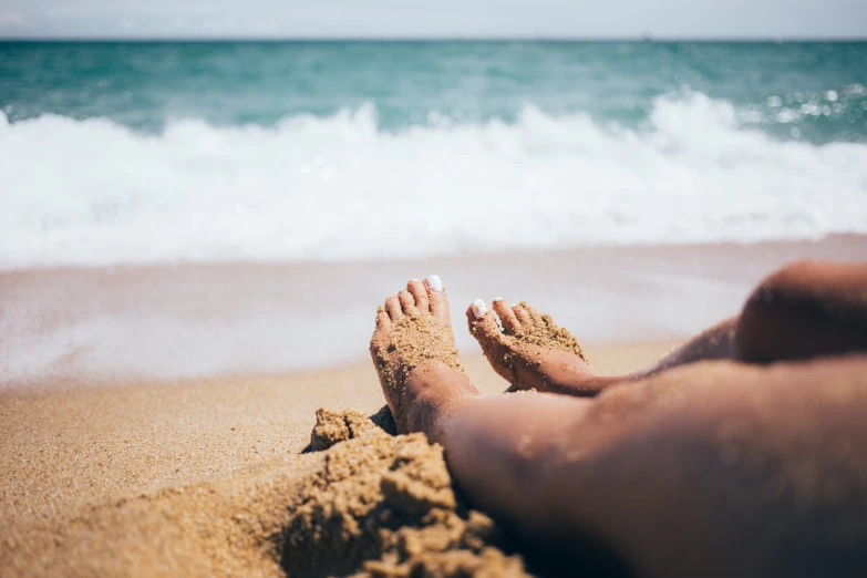 barefoot person's feet buried in sand near the ocean