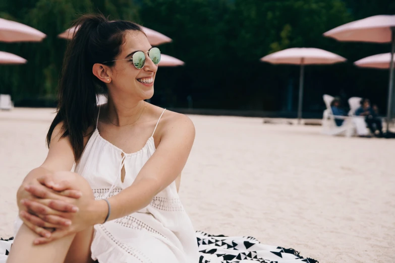 a woman sitting on a towel at the beach with some umbrellas