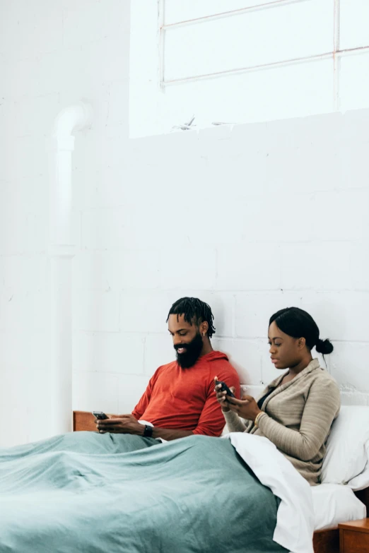 two people sitting on a bed using cell phones