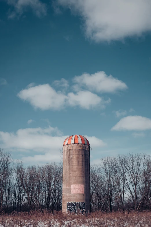 an old concrete tower in a field that has trees on both sides