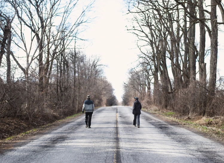 two people walking down the middle of a tree lined road