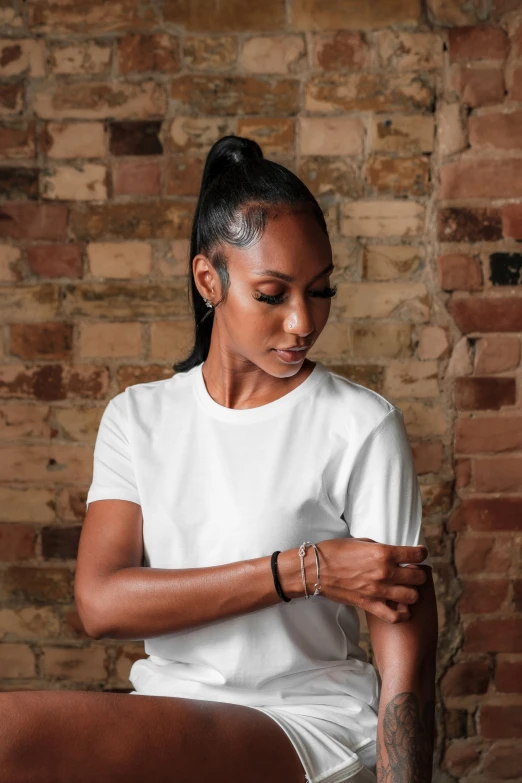 a black woman is looking down with her hands clasped and brick wall behind her