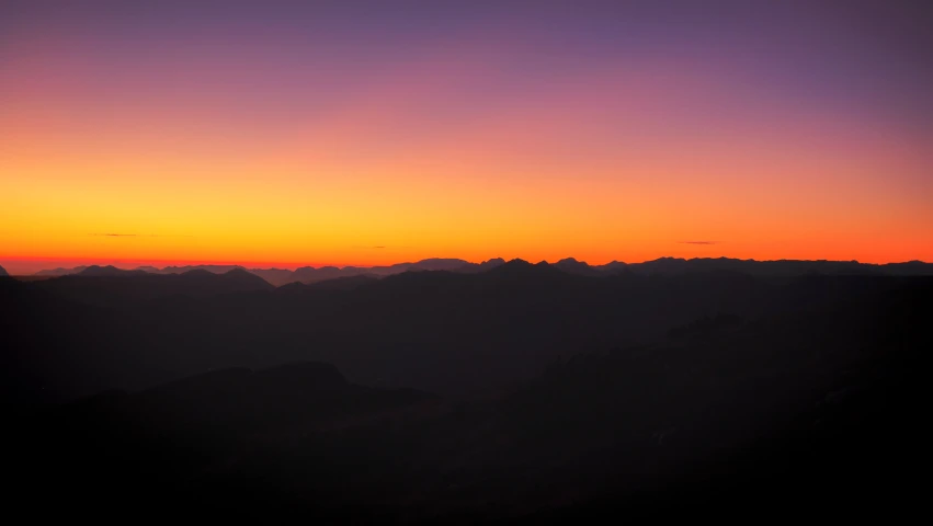 sunset over mountains with dark clouds and a lone plane in front