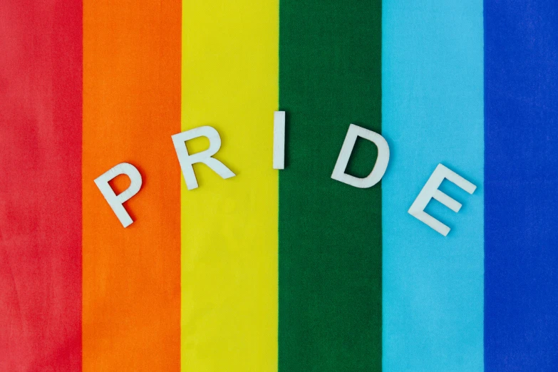 a close up s of a word pride spelled with cutout letters on a rainbow colored background