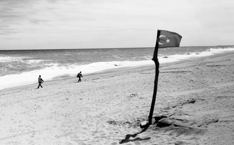 two people walking on the beach with a flag