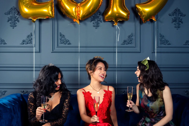 three beautiful women sitting on a blue couch holding champagne glasses