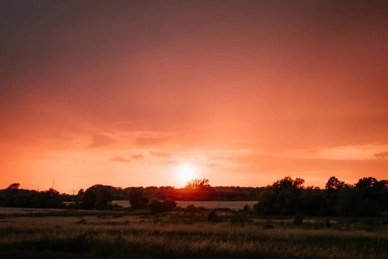 a lone train passes the setting sun in an orange sky