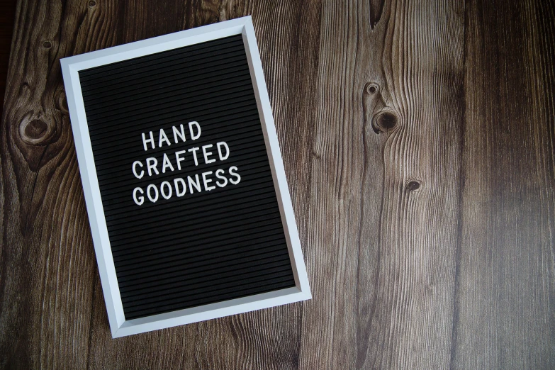 a hand crafted goodness sign laying on top of a wooden floor