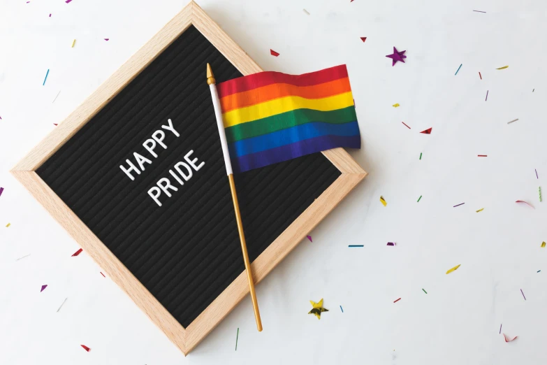 a black sign with white writing that says happy pride and a rainbow flag on top