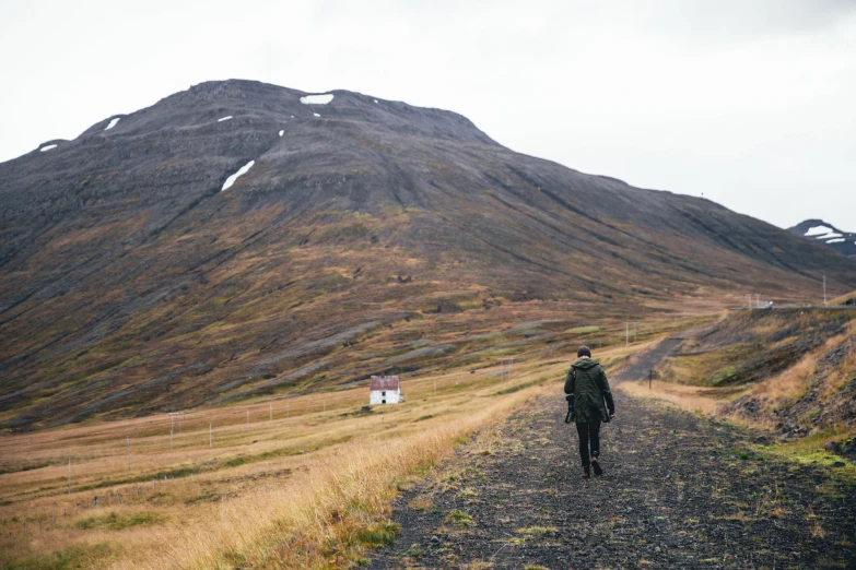 a man is walking along a dirt path towards a huge hill