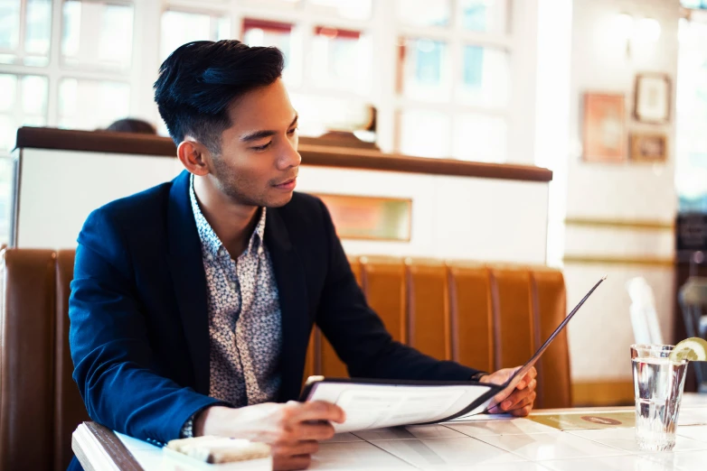 young man sitting at table in restaurant reading newspaper