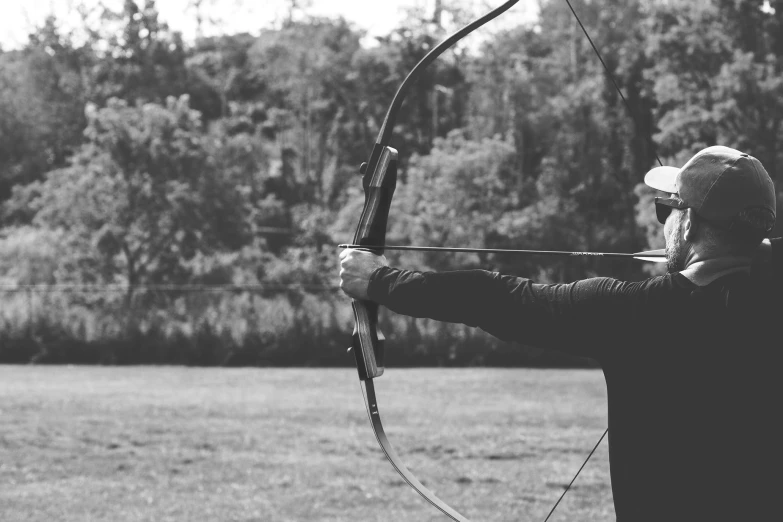 a man with a hat, jacket and black shirt aiming an arrow