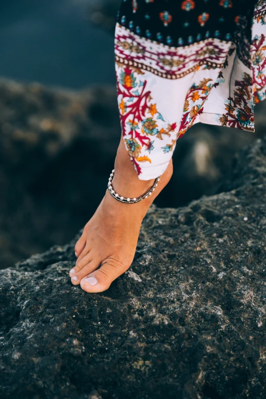 barefoot barefooted woman on rock by water in patterned dress