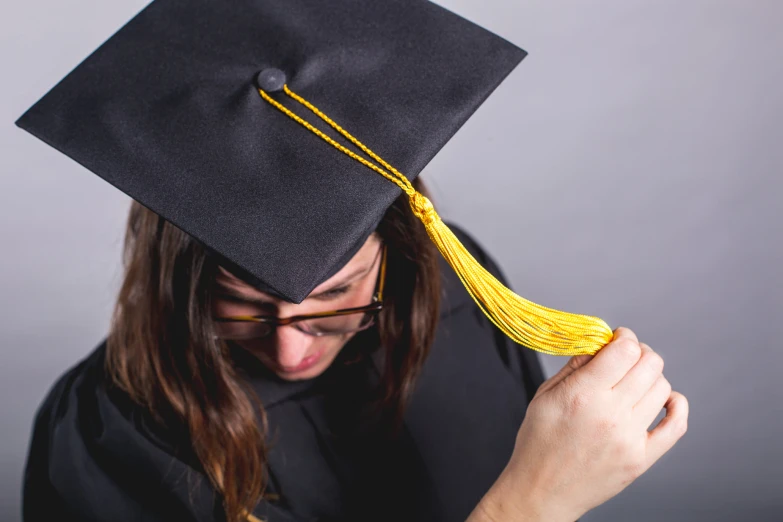 a man in a graduation gown holds up his cap