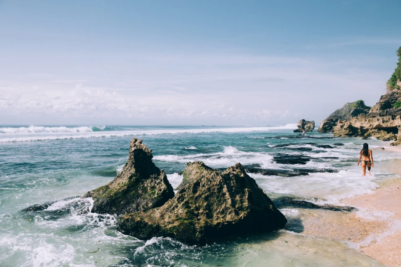 woman walking along beach near ocean with rock formations