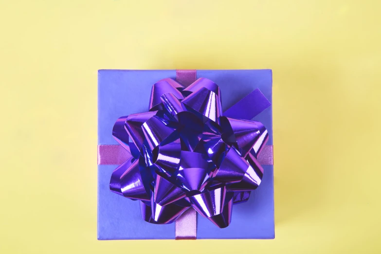 a shiny present wrapped in purple ribbon on yellow background