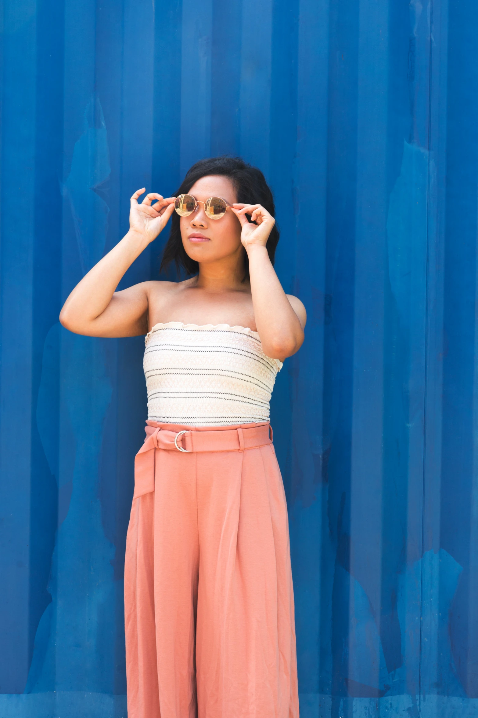 a person with sunglasses standing by a blue wall