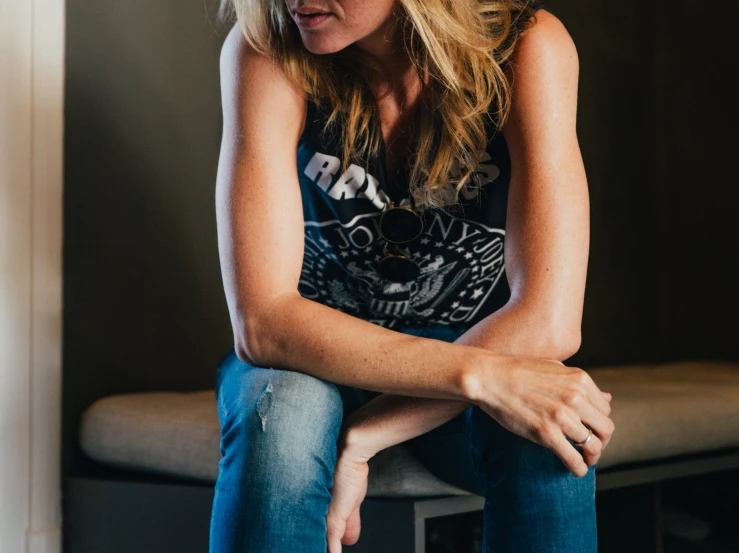 a woman wearing jeans sits on a bench