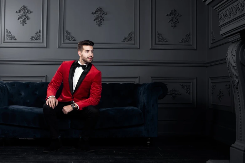 a young man wearing a red jacket, black bow tie and pants sitting on a blue couch