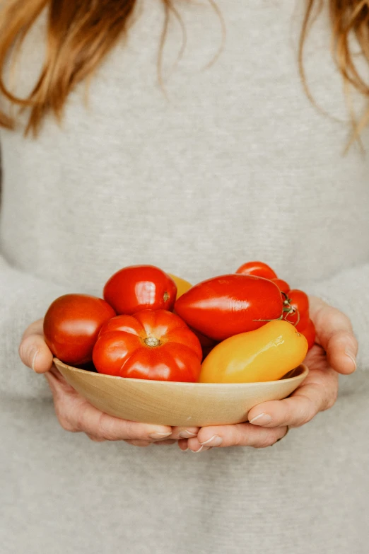 a person is holding a bowl with tomatoes and an onion