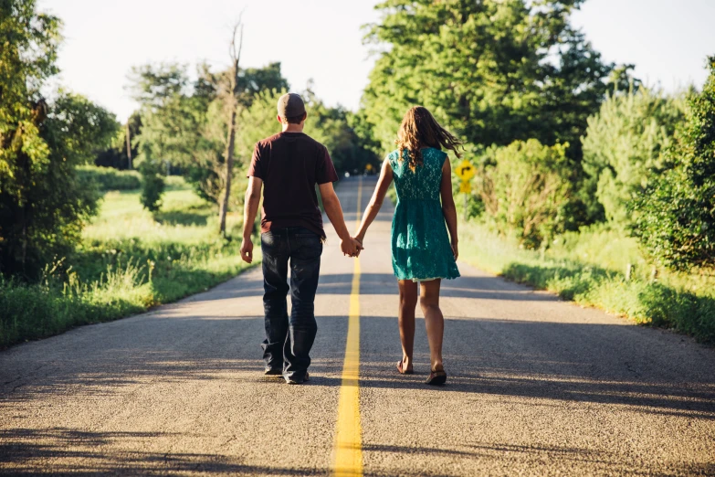 a man and woman walking down the road holding hands