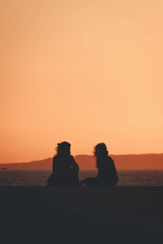 two women sitting on a wall, watching the sunset