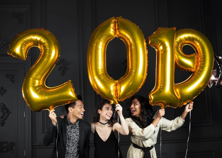 three women hold balloons in the shape of numbers to celete a new year