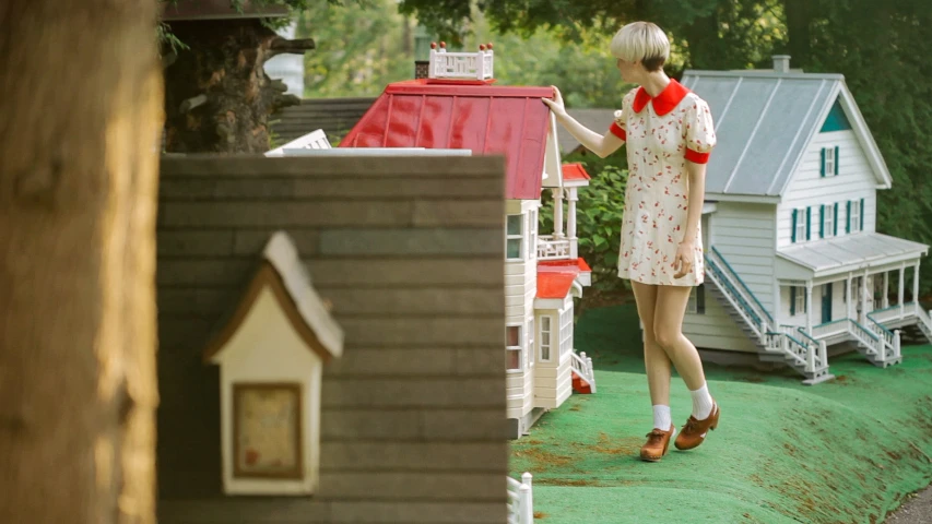 a woman standing on top of a green field next to doll houses