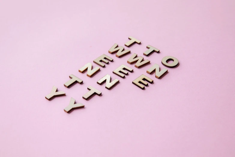 four wooden cutouts spelling out letters on a pink surface