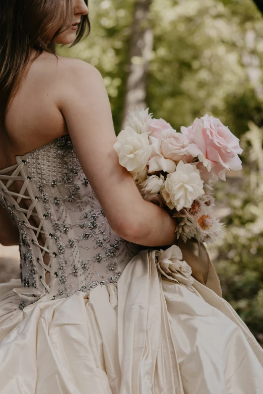 a woman in white dress holding flowers next to trees