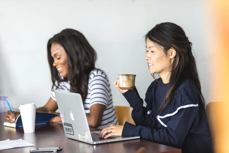 three women are sitting at a table with laptops and coffee