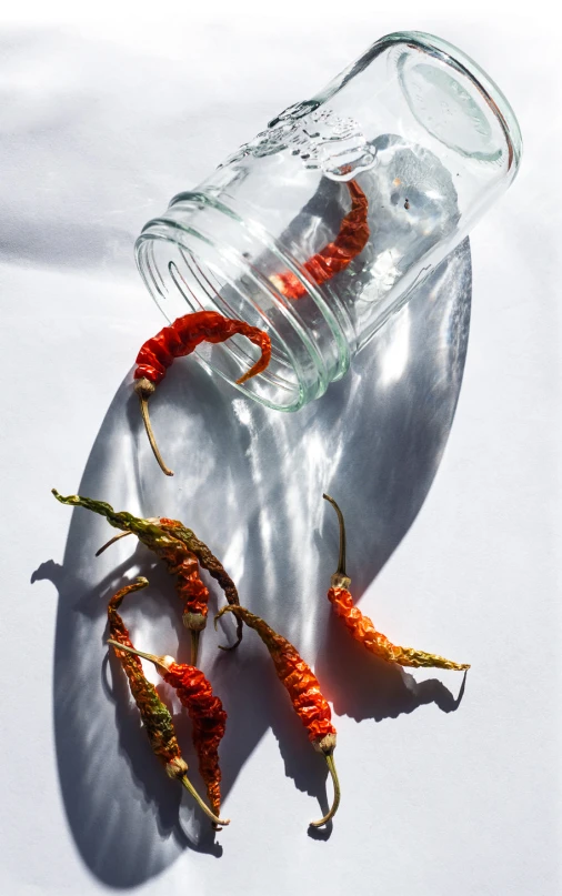 some red peppers that have fallen out of a glass bottle