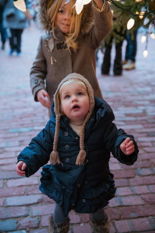 two s wearing hats and scarves and holding onto a christmas tree