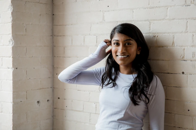 a young woman leaning against a white brick wall smiling at the camera