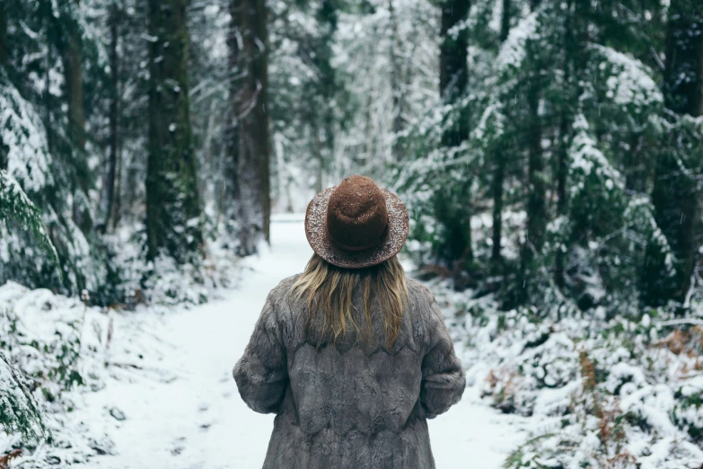 a woman wearing a hat walking through a snowy forest
