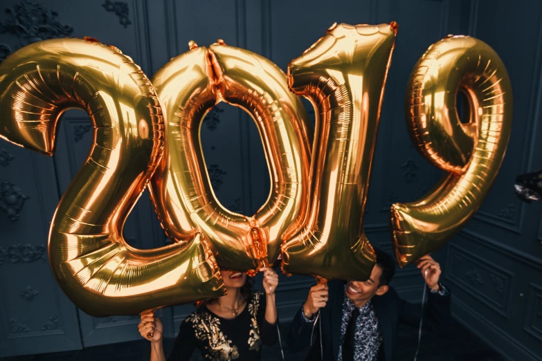 two girls are holding gold letters while wearing large balloons