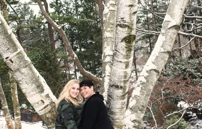 a young couple in black and white are hugging by a snowy tree