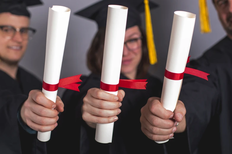 three graduates hold graduation hats and diplomas